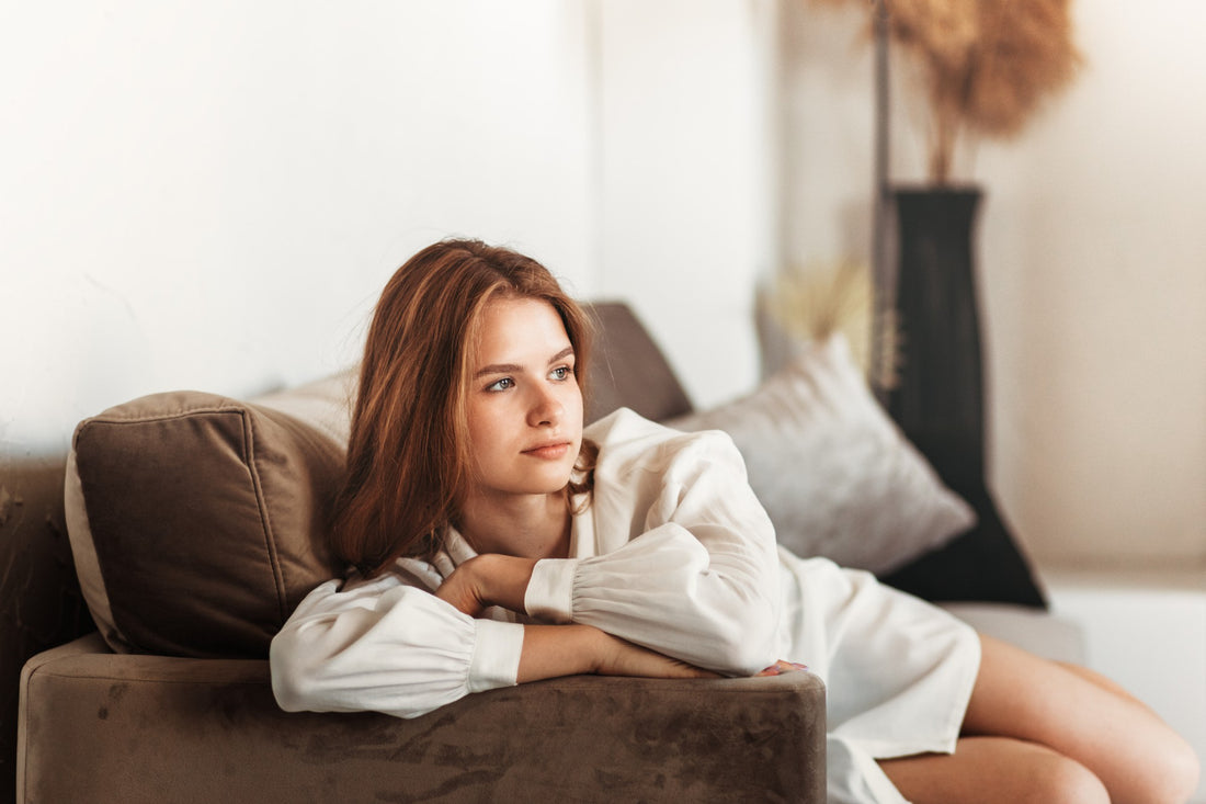 Young beautiful girl with long hair in a white shirt sits on a couch in the bedroom in the morning