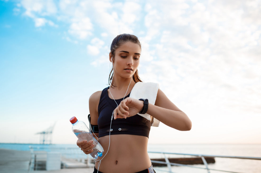 A woman holding a water bottle and looking at her smart watch