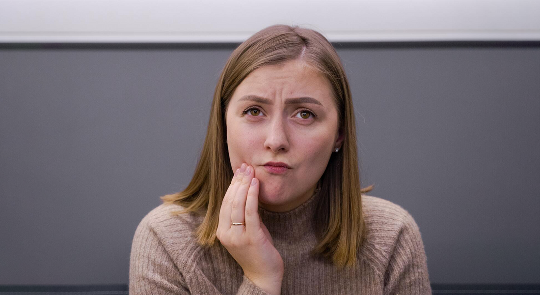 A woman who experiences a tooth ache and touching her cheek