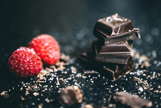 Multiple cubes of dark chocolate and two raspberries