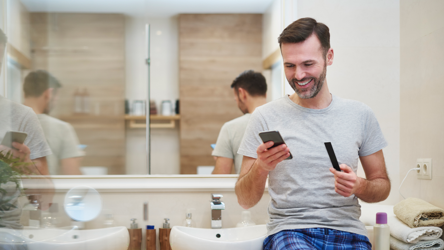 a man holding a phone and a vivoo urine strip in the bathroom